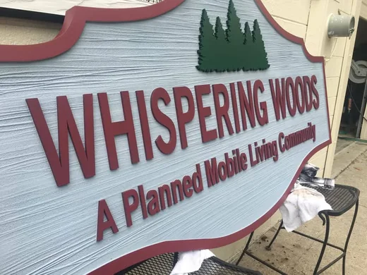 Whispering Woods dimensional community entrance sign with woodgrain background and raised lettering